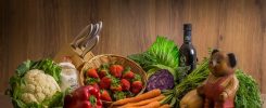 Arrangement of fresh vegetables and fruits on a wooden table with kitchen essentials.